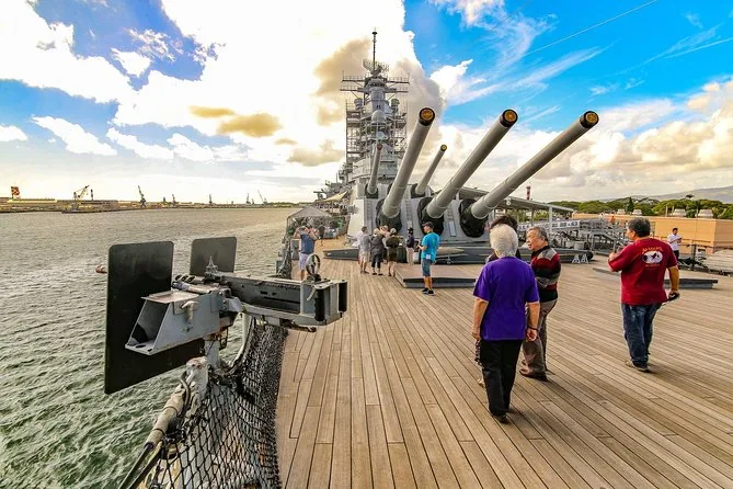 Visitatori che camminano sul ponte in teak della Missouri verso una torre con tre grossi cannoni