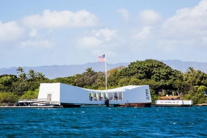 The white memorial seen from the side, lower in the middle than at the ends, with its flag and a USS Arizona BB 39 sign
