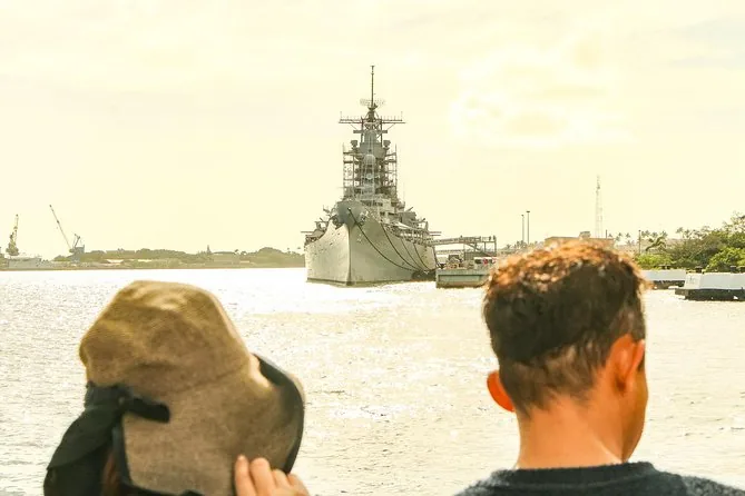 Two visitors, one holding on to a hat, looking across the water at the Battleship Missouri