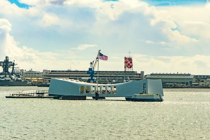 Il memoriale bianco della USS Arizona nel porto, con una nave da guerra grigia e una torre rossa e bianca sullo sfondo