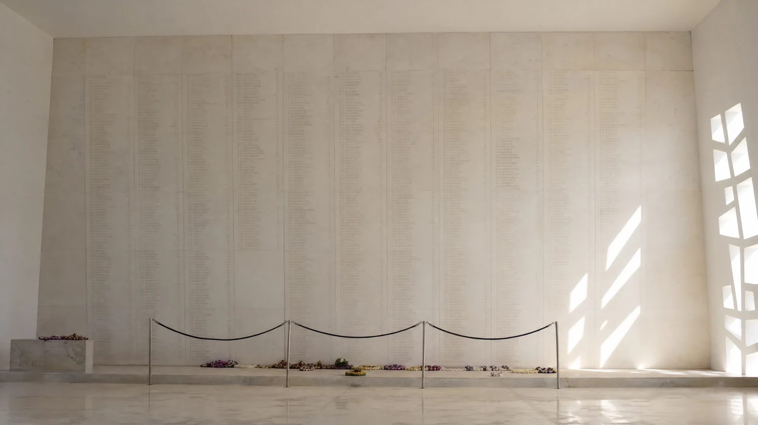 Die weiße Marmorwand des Gedenkraums im USS Arizona Memorial mit Blumen-Leis davor